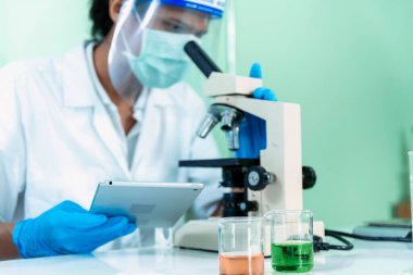 Indian Scientist man look into Microscope research in science laboratory. Asian biochemistry scientist using microscope in laboratory chemistry labs. Covid-19 medical research scientific experiment