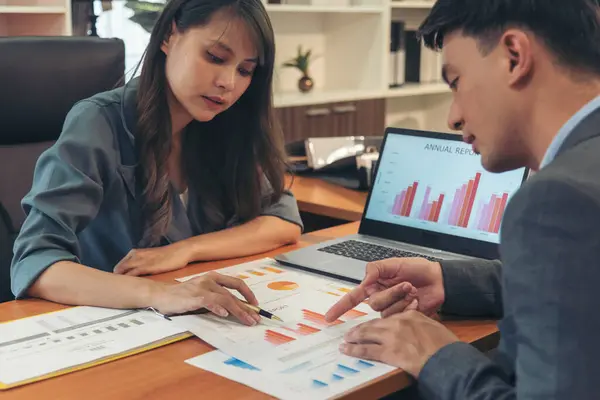 Two businesspeople meeting team discuss using laptop look at financial graph chart in office desk. Two young businessman reading Planning analyze marketing infographic. Partners team working together