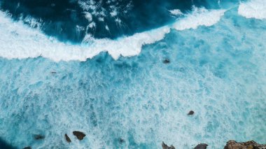 Turkuaz okyanus suyu beyaz dalga deseni derin mavi denize sıçrıyor. Deniz manzaralı karanlık okyanus dalgaları kayalara çarpıyor. Yazın açık deniz sahillerinde tropik deniz plajı. Su yüzeyindeki mavi dalga deseni