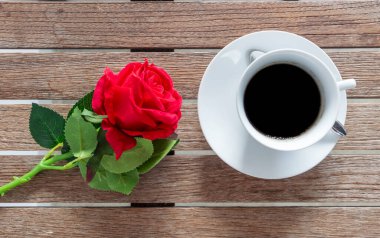 Masa üstü sade kahve fincanı ahşap masa arkasında kırmızı gül ve boş fotokopi alanı. Espresso kafeinli sıcak kahve bardağını kafede vurdu. Kafeteryada fotokopi alanı olan koyu kafeinli bir içecek.