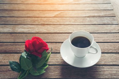 Masa üstü sade kahve fincanı ahşap masa arkasında kırmızı gül ve boş fotokopi alanı. Espresso kafeinli sıcak kahve bardağını kafede vurdu. Kafeteryada fotokopi alanı olan koyu kafeinli bir içecek.