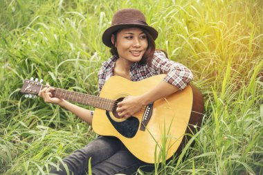 Yeşil parkta akustik gitar çalan genç kadınlar. Evde akustik gitar enstrümanı çalan bir kadın, güzel doğada genç Asyalı müzisyen kız yaşam tarzı. Mutlu gitarist