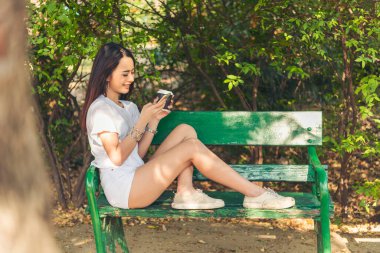 Asyalı kadın yeşil parkta tek kullanımlık sıcak kahve bardağı tutarken akıllı telefon kullanıyor. Banner Happy rahat Asyalı kadın açık hava bahçesinde gülümsüyor. Genç kadınlar fotokopi odasıyla doğanın tadını çıkarıyor