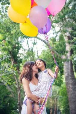 Dikey Mutluluk Anne kızı birlikte balon oynuyor yeşil bahçe parkı açık hava yaşam tarzı. Mutlu bir aile. İki insan eğlenmeyi sever. Anne çocukluk eli dışarıda renkli balonlar tutuyor.