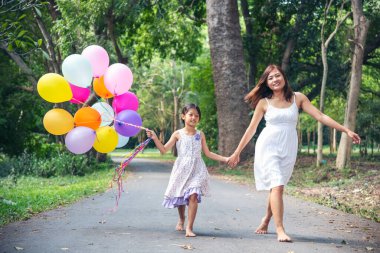 Mutlu bir aile iki insanın eğlencesine gülümser. Anne çocukluk eli dışarıda renkli balonlar tutuyor. Mutluluk anne kızı birlikte balon oynuyor yeşil bahçe parkında açık hava yaşam tarzında
