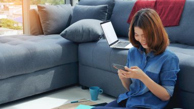 Asyalı kadınlar evdeki küçük ofis masasından akıllı telefon aracılığıyla konuşurlar. Genç Asyalı Kadın elleri telefon teknolojisi yaşam tarzını tutuyor. Mutlu kadın arayan kişi ev ofisinde dijital akıllı telefon kullanıyor.