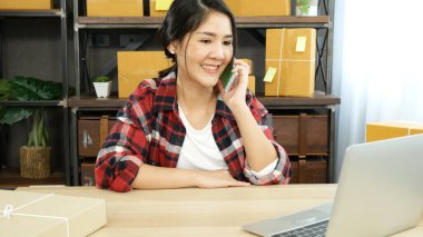 Çevrimiçi satıcı girişimci genç Asyalı kadın telefonla arıyor, internetten siparişleri kontrol ediyor. Kadının biri çek deposunu arıyor, teslimat paketlerini getiriyor. Asyalı kadın ev ofisinde küçük bir iş kurdu