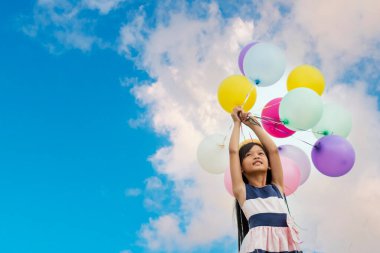 Yeşil çayır üzerinde koşan balonlar tutan neşeli şirin kız beyaz bulut ve mutlulukla mavi gökyüzü. Hava balonları tutan eller doğum günü partisinde oynar. Mutlu zamanlar yaz mevsimi açık havada.