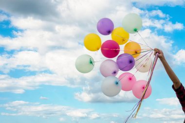 Balon tutan neşeli güzel kadın yeşil parktaki büyük ağacın altında mutlu mesut oturuyor. Kadın Eller 'in elinde canlı hava balonları var. Doğum günü partisinde oynuyorlar. Mutlu yaz mevsimi açık havada.