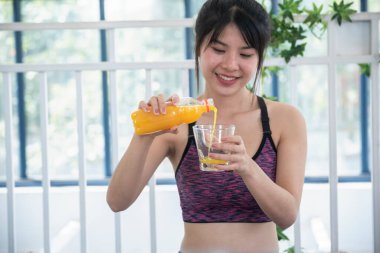 Kadın elleri soğuk portakal suyu tutuyor taze meyve suyu içiyor. Asyalı kadınlar güler, kameralı sağlık hizmetleri yaşam tarzına bakarlar. Güzel bir kadın kokteyl şişesinden portakal suyu dolduruyor.