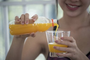 Asyalı kadınlar güler, kameralı sağlık hizmetleri yaşam tarzına bakarlar. Kadın elleri soğuk portakal suyu tutuyor taze meyve suyu içiyor. Güzel bir kadın kokteyl şişesinden portakal suyu dolduruyor.