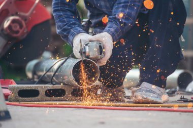 Çilingir kaynak makinesi kullanmış. Metal işlemleri kesmiş. İnşaat işçisi elleri kaynak makineleri ile metal kıvılcımlar saçıyor. Erkeklerin elleri koruyucu eldiven takar Alev metali, ateş demiri atölyesini keser