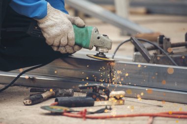 İnşaat işçisi elleri kaynak makineleri ile metal kıvılcımlar saçıyor. Erkek elleri koruyucu eldiven giyer. Alev metali, ateş demiri atölyesini keser. Çilingir kaynak makinesi kullanarak metal işlemini kesti