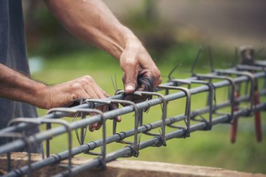 İnşaatçıların elleri çelik telleri büküyor beton işçiliğini destekliyor. Kerpeten kullanan işçi elleri demir tel kullanıyor. Açık hava işçisi, tel bükme pensesi kullanıyor, inşaat işi yapıyor.
