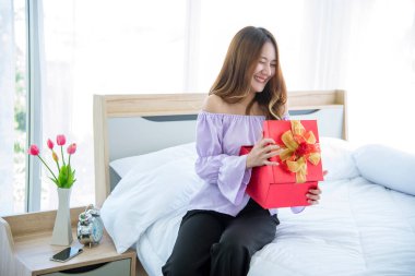 Kadın sürprizi Noel arifesinde hediye kutusunu aldı. Asyalı bir kadın Noel ağacının altında gülen yüzlü bir hediye kutusu tutuyor. Kadın eli hediyeyi paketler. Mutlu noeller Yeni yıl konsepti