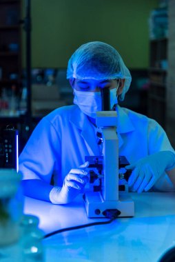 Laboratuvardaki dikey bilimadamı kadınlar, mavi açık siyah arka planlı biyoloji kimyasını araştıran mikroskop tıbbi testine bakıyorlar. Erkek teknisyen laboratuarı Kimya Tıbbi Araştırmalarını analiz ediyor