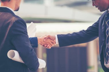 İnşaat mühendisi takımları el sıkışırken inşaat alanında kask takıyor. Foreman Endüstri Projesi Mühendis ekip çalışması. İki Asyalı mühendis takımı el sıkışıyor.