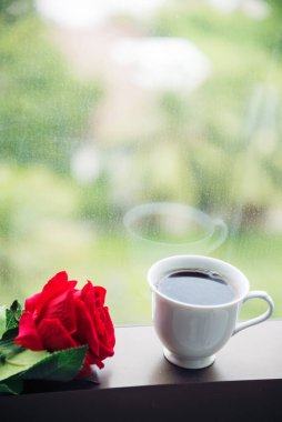 Masa üstü sade kahve fincanı ahşap masa arkasında kırmızı gül ve boş fotokopi alanı. Espresso kafeinli sıcak kahve bardağını kafede vurdu. Kafeteryada fotokopi alanı olan koyu kafeinli bir içecek.