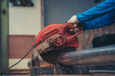 İnşaat işçisi elleri kaynak makineleri ile metal kıvılcımlar saçıyor. Erkek elleri koruyucu eldiven giyer. Alev metali, ateş demiri atölyesini keser. Çilingir kaynak makinesi kullanarak metal işlemini kesti