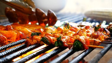 Barbekü ızgara et çubuğu ateşte, dışarıda da sıcak kömür var. Parti için domuz pastırmalı sosisli ızgara piknik. Izgara domuz eti ateşte yanıyor.