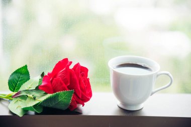 Masa üstü sade kahve fincanı ahşap masa arkasında kırmızı gül ve boş fotokopi alanı. Espresso kafeinli sıcak kahve bardağını kafede vurdu. Kafeteryada fotokopi alanı olan koyu kafeinli bir içecek.