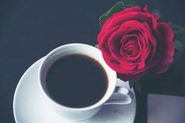 Masa üstü sade kahve fincanı ahşap masa arkasında kırmızı gül ve boş fotokopi alanı. Espresso kafeinli sıcak kahve bardağını kafede vurdu. Kafeteryada fotokopi alanı olan koyu kafeinli bir içecek.