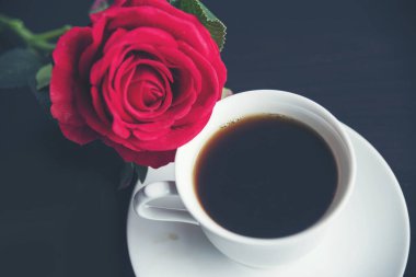 Masa üstü sade kahve fincanı ahşap masa arkasında kırmızı gül ve boş fotokopi alanı. Espresso kafeinli sıcak kahve bardağını kafede vurdu. Kafeteryada fotokopi alanı olan koyu kafeinli bir içecek.