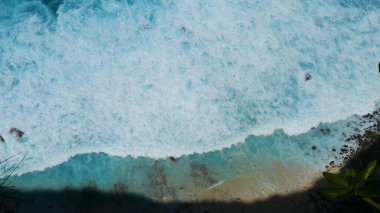 Turkuaz okyanus suyu beyaz dalga deseni derin mavi denize sıçrıyor. Deniz manzaralı karanlık okyanus dalgaları kayalara çarpıyor. Yazın açık deniz sahillerinde tropik deniz plajı. Su yüzeyindeki mavi dalga deseni