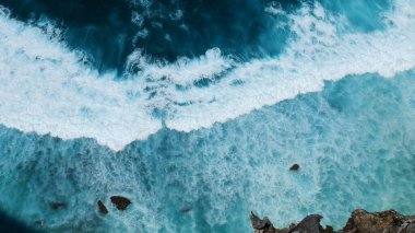 Turkuaz okyanus suyu beyaz dalga deseni derin mavi denize sıçrıyor. Deniz manzaralı karanlık okyanus dalgaları kayalara çarpıyor. Yazın açık deniz sahillerinde tropik deniz plajı. Su yüzeyindeki mavi dalga deseni