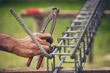 Kerpeten kullanan inşaat işçisi elleri demir tel kullanıyor. Açık hava işçisi, kerpeten kullanıyor, inşaat işlerinde çalışıyor. Erkekler elleri büküyor çelik telleri kesiyor beton işçiliğini destekliyor.
