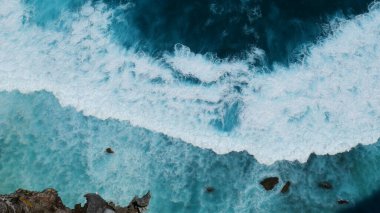 Turkuaz okyanus suyu beyaz dalga deseni derin mavi denize sıçrıyor. Deniz manzaralı karanlık okyanus dalgaları kayalara çarpıyor. Yazın açık deniz sahillerinde tropik deniz plajı. Su yüzeyindeki mavi dalga deseni