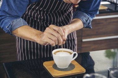 Kahve barmeni espresso doldurur ve sıcak kahve fincanı yapar. İtalyan kafeteryasında sütlü kapuçino. Kahvecinin ellerini kapat. Müşteri kafeteryası için kahverengi latte sanatı yap..