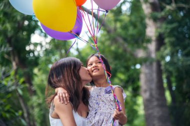 Mutlu anne kız, yeşil bahçe parkında birlikte balon oynuyor. Mutlu bir aile iki insanın eğlencesine gülümser. Anne çocukluk eli dışarıda renkli balonlar tutuyor.
