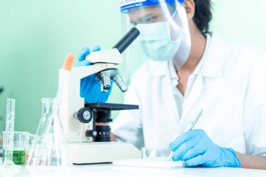 Bilim adamı bilim laboratuarındaki mikroskop araştırmalarını inceliyor. Asyalı bilim adamı laboratuvar kimya laboratuvarlarını arıyor. Covid-19 Coronavirus biyokimya araştırma deneyi aşı konsepti