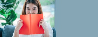 Banner, Asyalı kadın kitap okuyor oturma odasında kitap tutuyor. Banner Young kadın açık kitap boş zihin okuyor. Mutluluk güzellik insanı gülümsüyor. Fotokopi alanıyla mutlu zaman geçiriyor.
