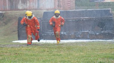 Firefighter Rescue team training in fire fighting extinguisher. Firefighter teamwork fighting with flame using fire hose chemical water foam spray engine. Fireman wear hard hat, safety suit uniform