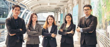 İş adamlarından oluşan Banner Portre Grubu modern şehir arka planındaki kameraya gülümseyen kollarını kavuşturdu. Banner Happy takımları ortaklığı. İş adamları takım çalışması kopyalama alanı ile ayakta