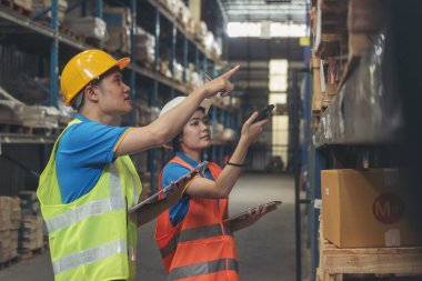 Depo yönetimi stok envanterini kontrol ediyor. Asyalı kadın işçi kadın barkod tarayıcı kullanıyor. Mal raflarını tarıyor ve listeyi panoya yazıyor. Ekip çalışması lojistik personeli ürün depolama envanterini sayıyor