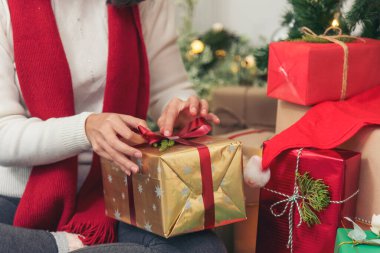 Kadın eli hediyesini sıcak oturma odasına sarın. Noel ağacının altında hediye paketi yapan bir kadın. Asyalı kadın dekoratif balo balosu Noel ağacı Noel 'de kış mevsimi kutlamalarında