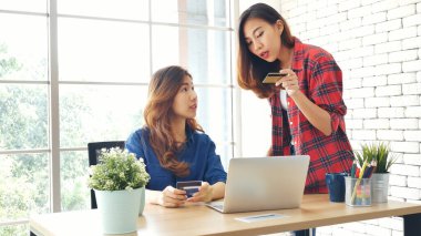 İki arkadaş internetten alışveriş yapıyor. İnternet sitesinde bilgisayardan alışveriş yapıyor. Gülümseyen yüzlü, mutlu. İnternetten bilgisayar alışverişi yapan mutlu Asyalı kadınlar, yeni konsept ödeme