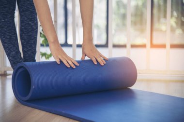 Kadın elleri yoga antrenman odasında jimnastik zemininde yoga minderini sardı. Egzersiz yapan kadın, köpüklü yoga paspası saran elleri kapıyor. Kadın yalınayak evde spor yapıyor sağlıklı yaşam tarzı konsepti