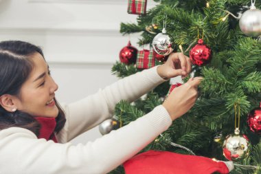 Kadın elleri Noel ağacını süslüyor kırmızı top, takı, kar taneciği. Kırmızı topu tutan elleri kapatın. Mücevher süsleme. Asyalı kadın dekoratif balo balosu Noel ağacı Noel tatilini kutluyor