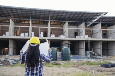 İnşaat mühendisi kadın işçi sanayisinde ekose gömlekli, beyaz kasketli, inşaat işçisi. Mimari mühendis kadın memur emlak projesine bakıyor.