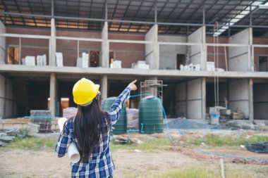 İnşaat mühendisi kadın işçi sanayisinde ekose gömlekli, beyaz kasketli, inşaat işçisi. Mimari mühendis kadın memur emlak projesine bakıyor.