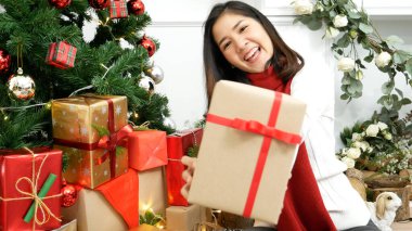 Kadın sürprizi Noel arifesinde hediye kutusunu aldı. Asyalı bir kadın Noel ağacının altında gülen yüzlü bir hediye kutusu tutuyor. Kadın eli hediyeyi paketler. Mutlu noeller Yeni yıl konsepti