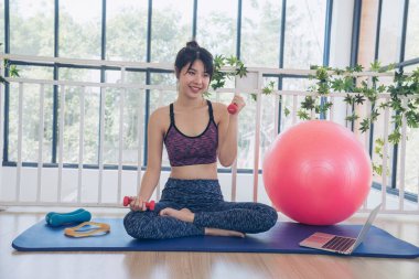 Beautiful Asian Women use dumbbell exercises for muscle-building home fitness. Women weight training smile use exercise pilates ball dumbbell. Beauty woman smiling sportswear on yoga mat home fitness