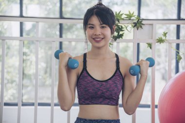 Beautiful Asian Women use dumbbell exercises for muscle-building home fitness. Women weight training smile use exercise pilates ball dumbbell. Beauty woman smiling sportswear on yoga mat home fitness
