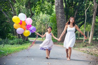 Mutlu bir aile iki insanın eğlencesine gülümser. Anne çocukluk eli dışarıda renkli balonlar tutuyor. Mutluluk anne kızı birlikte balon oynuyor yeşil bahçe parkında açık hava yaşam tarzında