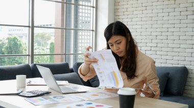 Ev ofis masasında dizüstü bilgisayar kullanan Asyalı kadın serbest yazar. Finansal grafik çizelgesi okuyan kadın pazarlama verilerini analiz ediyor. Ofiste çalışan Asyalı kadınlar, iş konuları, kahve fincanları.