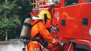 İtfaiyeci, itfaiye aracında yangın söndürücüyü söndürmek için ekipman hazırla. İtfaiyeci duman aleviyle savaşıyor. Yangın hortumu, tüp, kamyonda kimyasal köpük spreyi kullanıyor. İtfaiyeci sıkı bir şapka takıyor.